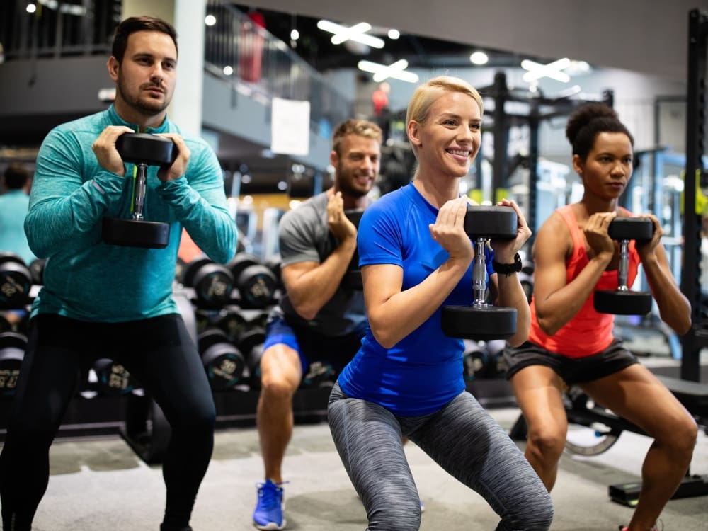 gym members squat with dumb bells during a small group training boot camp at freedom fitness gym in corpus christi