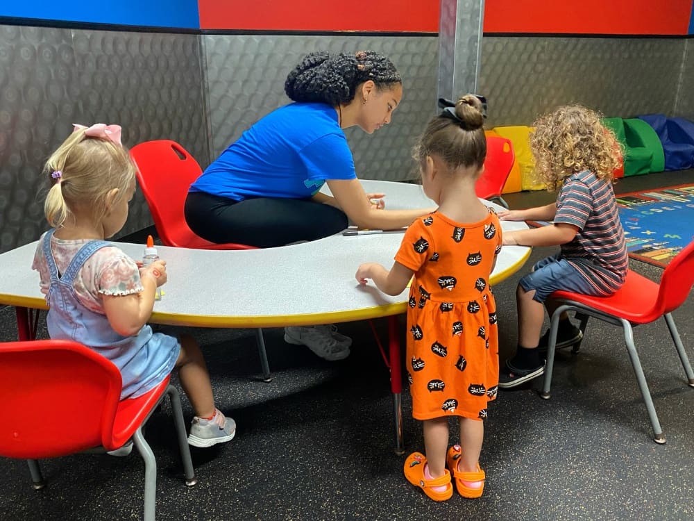 an onsite childcare worker helps kids with crafts at a gym near me