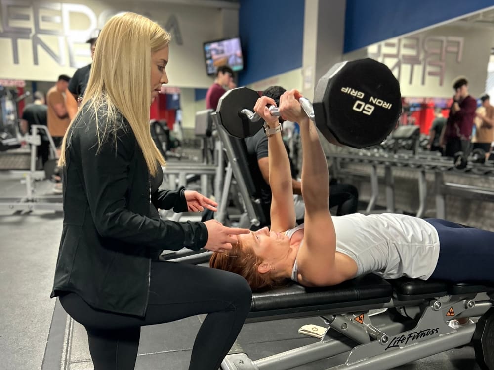 a gym member works with a personal trainer during a barbell lift at a corpus christi gym