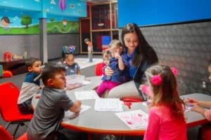 Daycare staff member reading to young children at a table inside a Corpus Christi gym.
