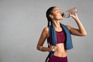 Person drinking water after a workout with a towel around their neck, highlighting the importance of hydration and recovery at our Corpus Christi gyms.