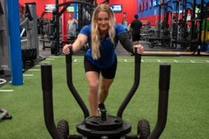 Freedom Fitness gym member pushing a weighted sled across indoor turf during a strength and conditioning workout.