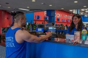 Freedom Fitness gym member checking in at the front desk before a workout while greeted by a friendly staff member.
