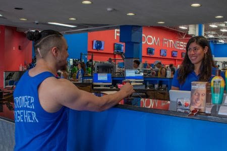 Freedom Fitness gym member checking in at the front desk before a workout while greeted by a friendly staff member.