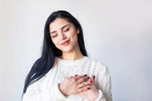 oung woman smiling with her hands over her heart, expressing gratitude and self-care.