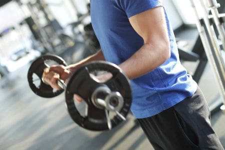 Person performing a barbell curl to build upper-body strength during a workout at our Corpus Christi gyms.